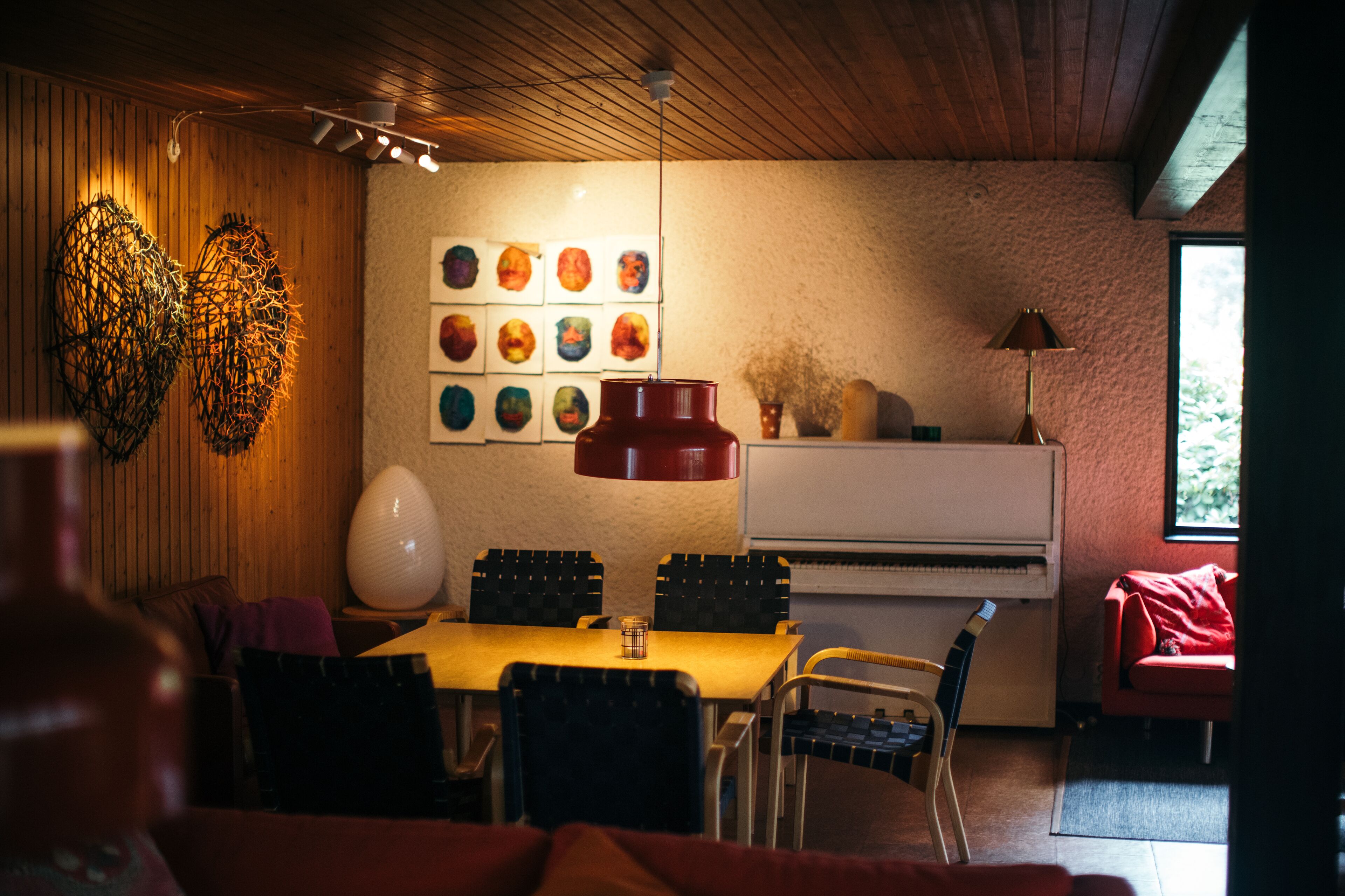 A dining area with a wooden ceiling, a table with chairs, a piano, and wall art.