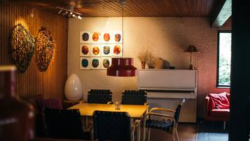 A dining area with a wooden ceiling, a table with chairs, a piano, and wall art.