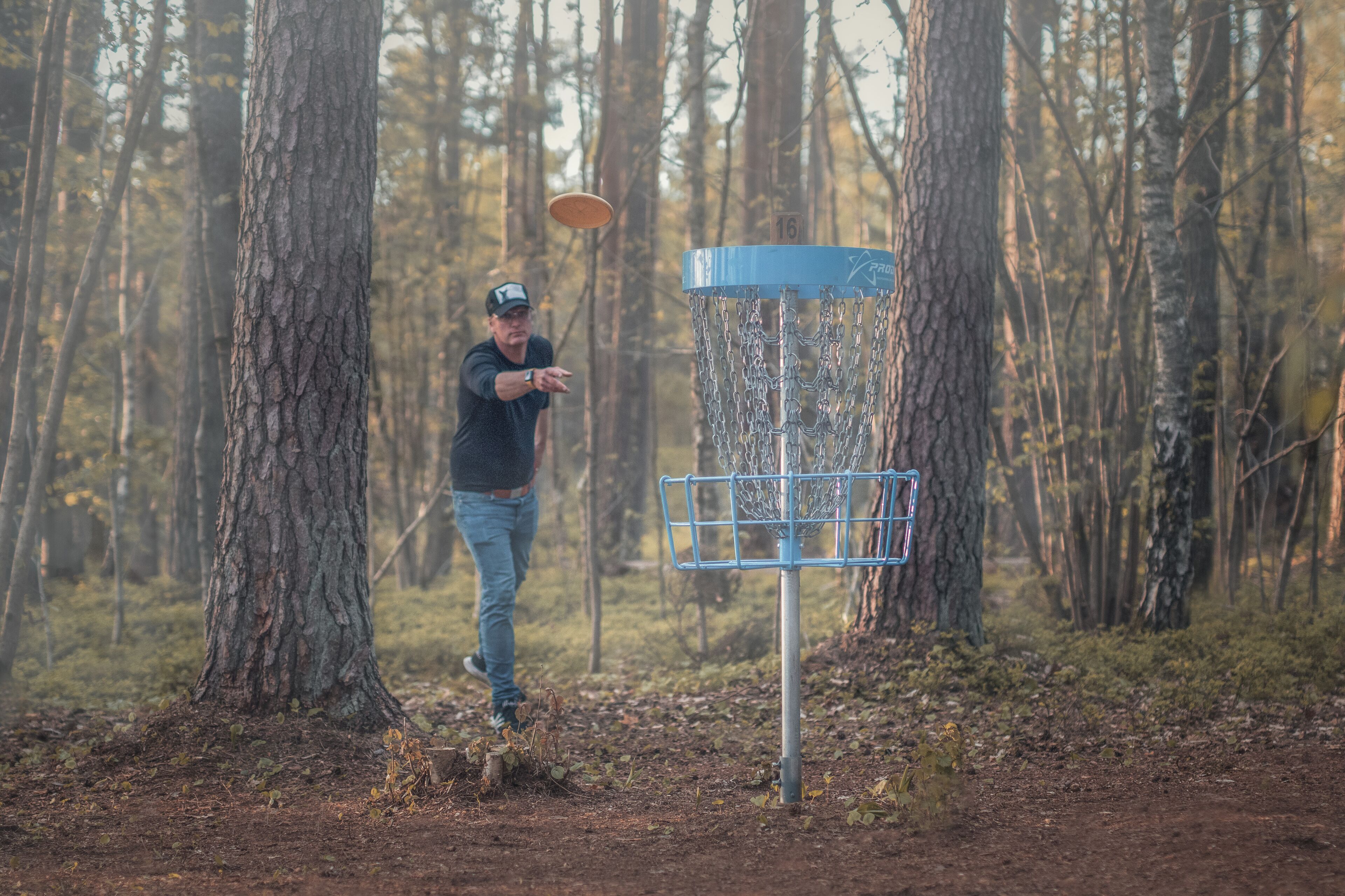 A person playing disc golf in a forested area with a metal basket.