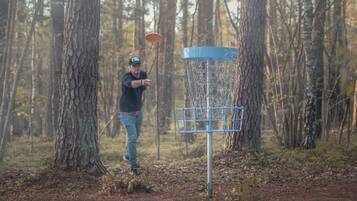 A person playing disc golf in a forested area with a metal basket.