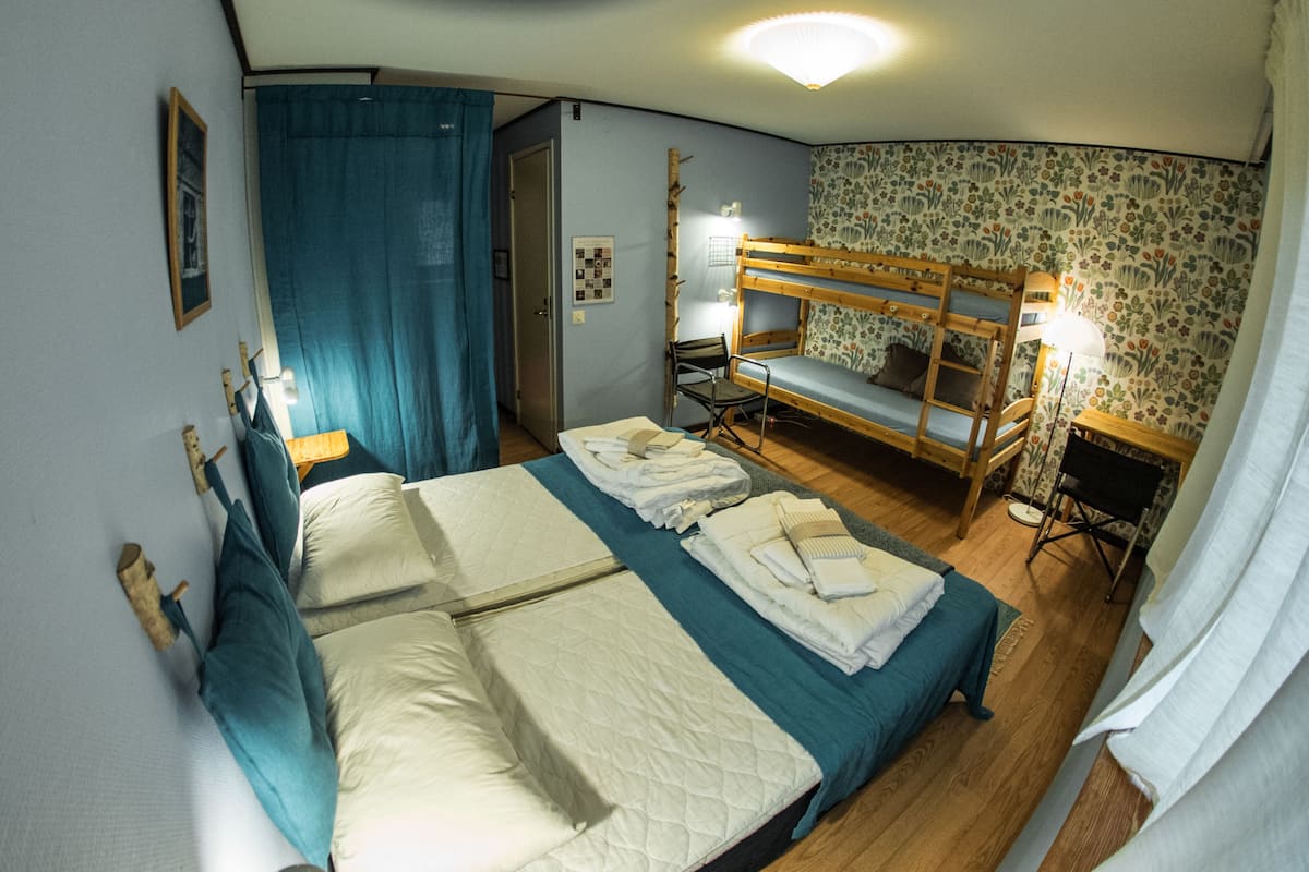 A room with two bunk beds, a desk, and a chair. There is a window with curtains, a lamp, and a framed picture on the wall.