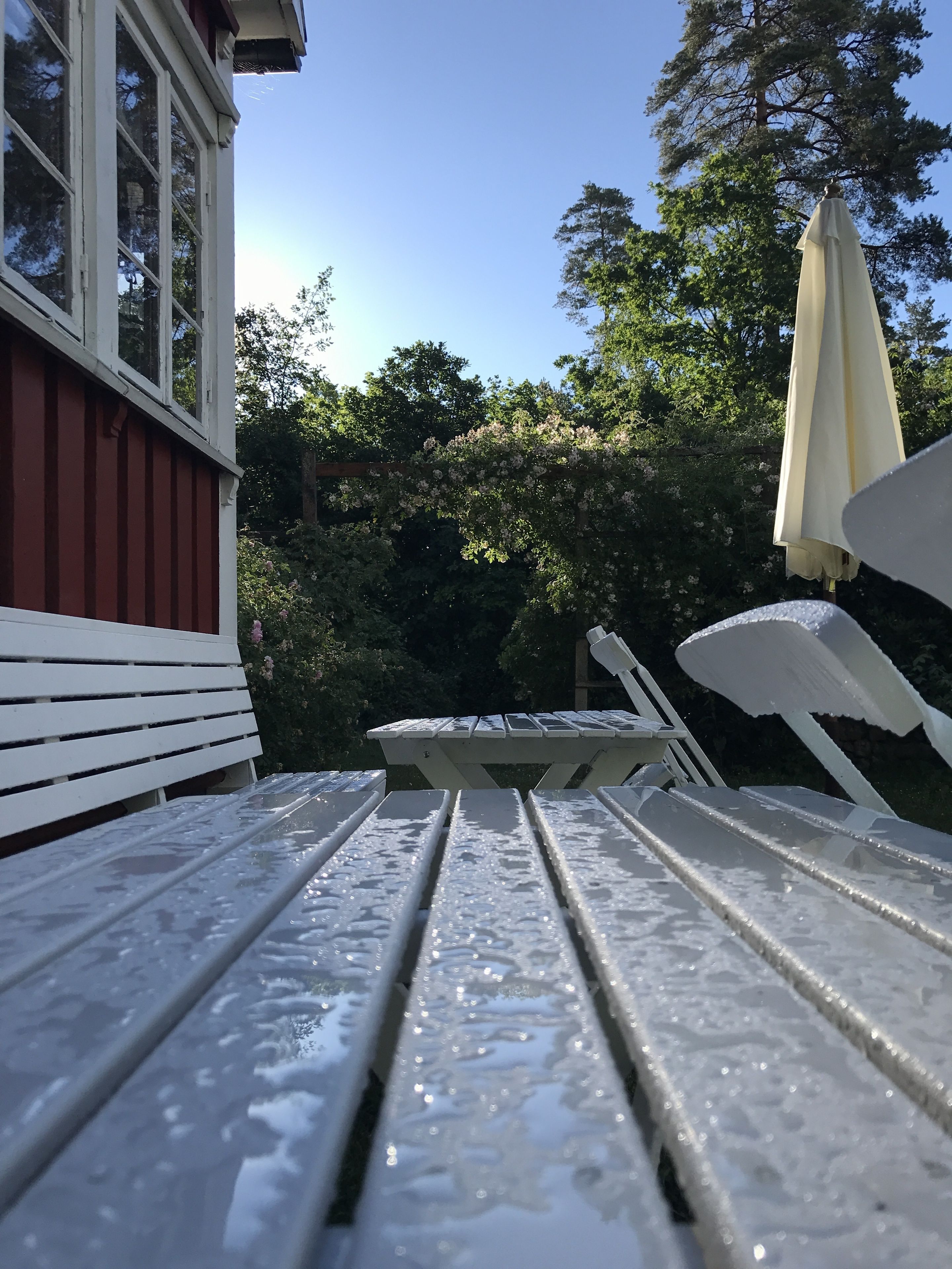 En terrasse med et hvidt bord og stole, en hvid parasol og en rød bygning i baggrunden.