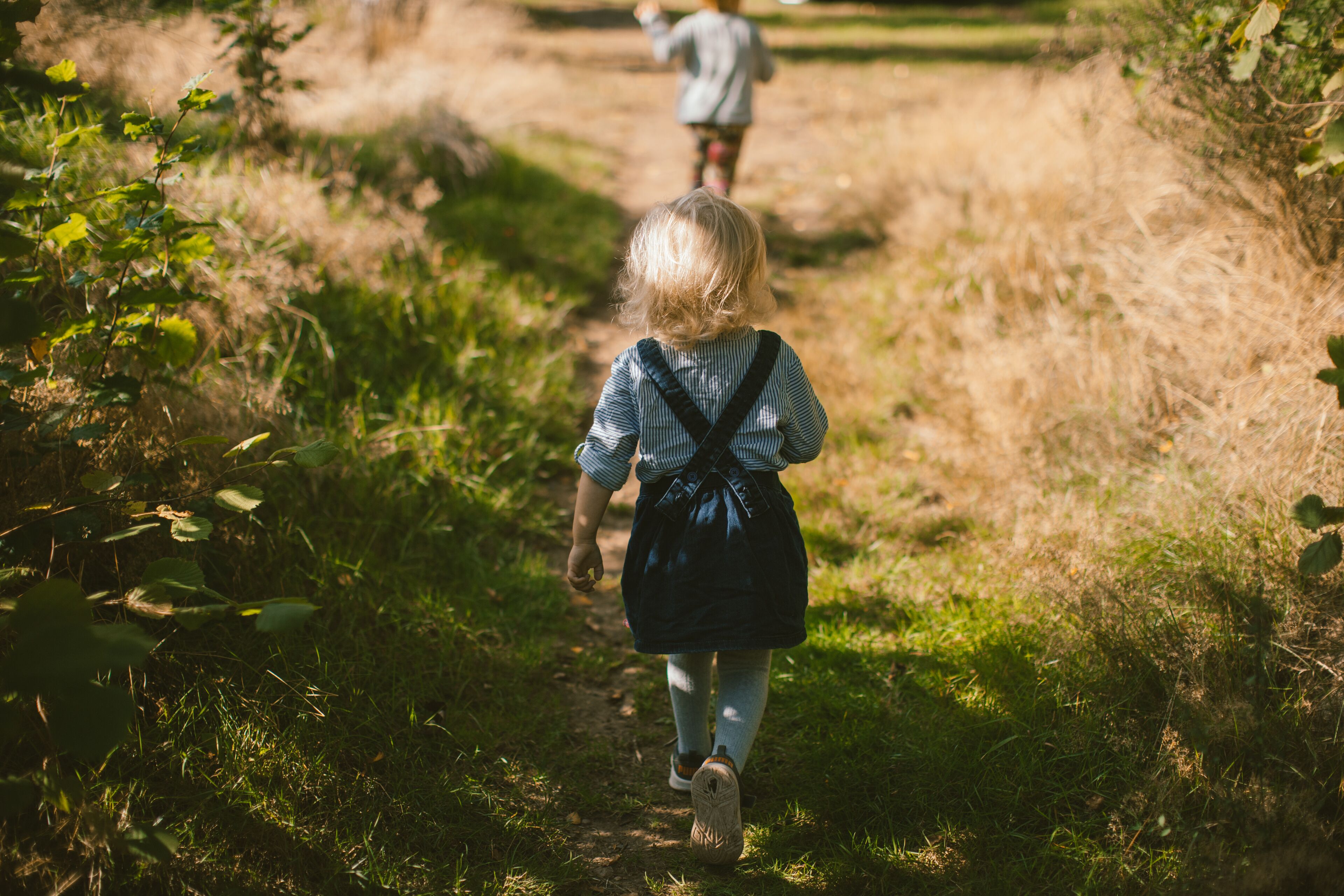 Un enfant qui marche sur un sentier herbeux, un sac à dos sur le dos.