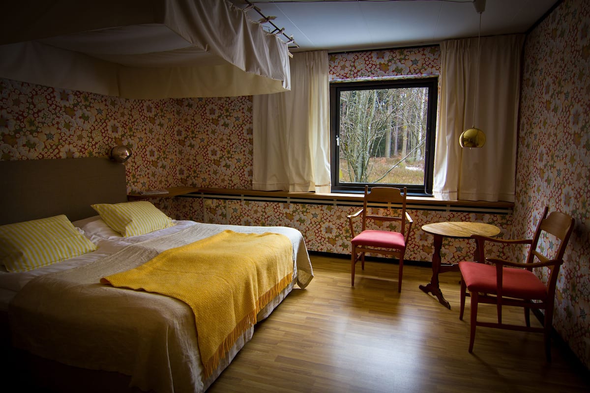 A bedroom with a bed, two chairs, a small table, and a window with curtains.