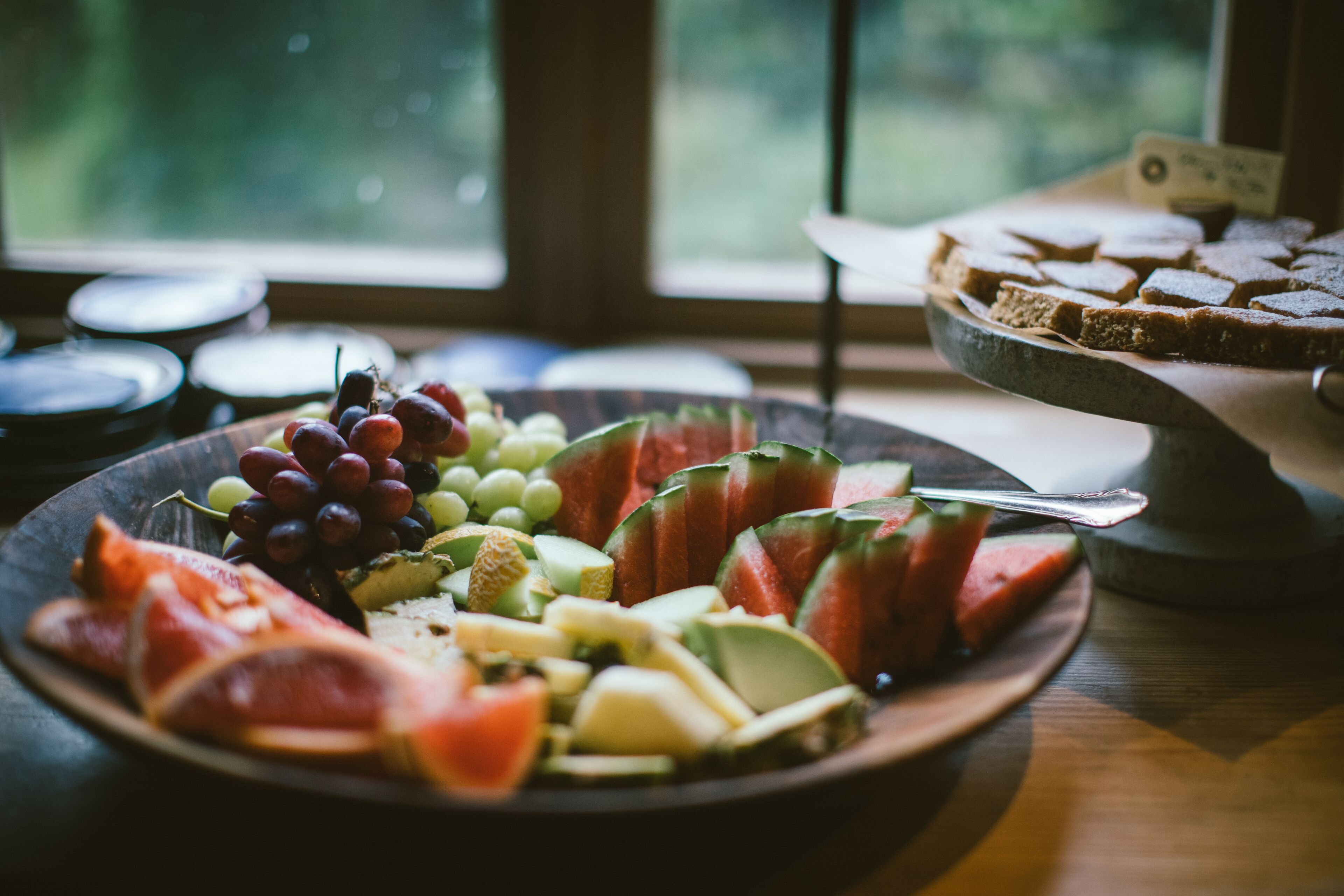 A plat de fruita amb síndria, raïms i formatge damunt un taulell de fusta a prop d'una finestra.