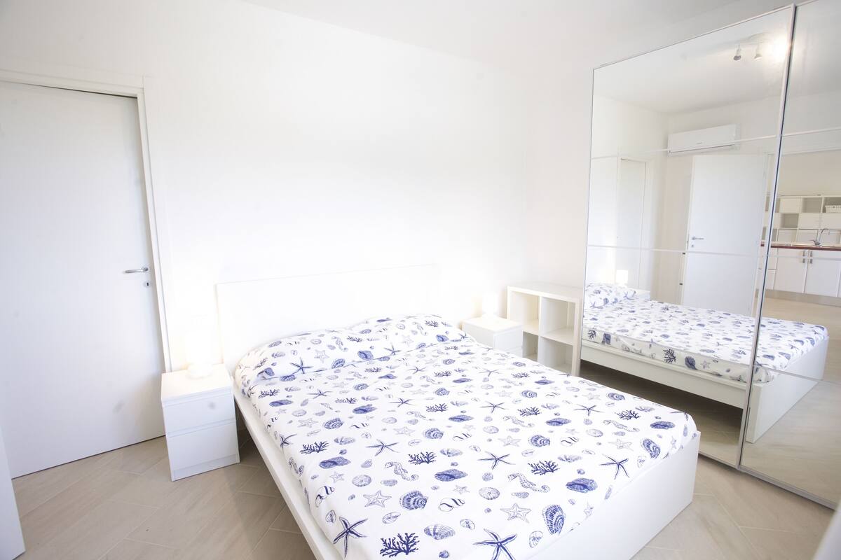 A bedroom with a bed, a nightstand, a mirror, and a wardrobe.