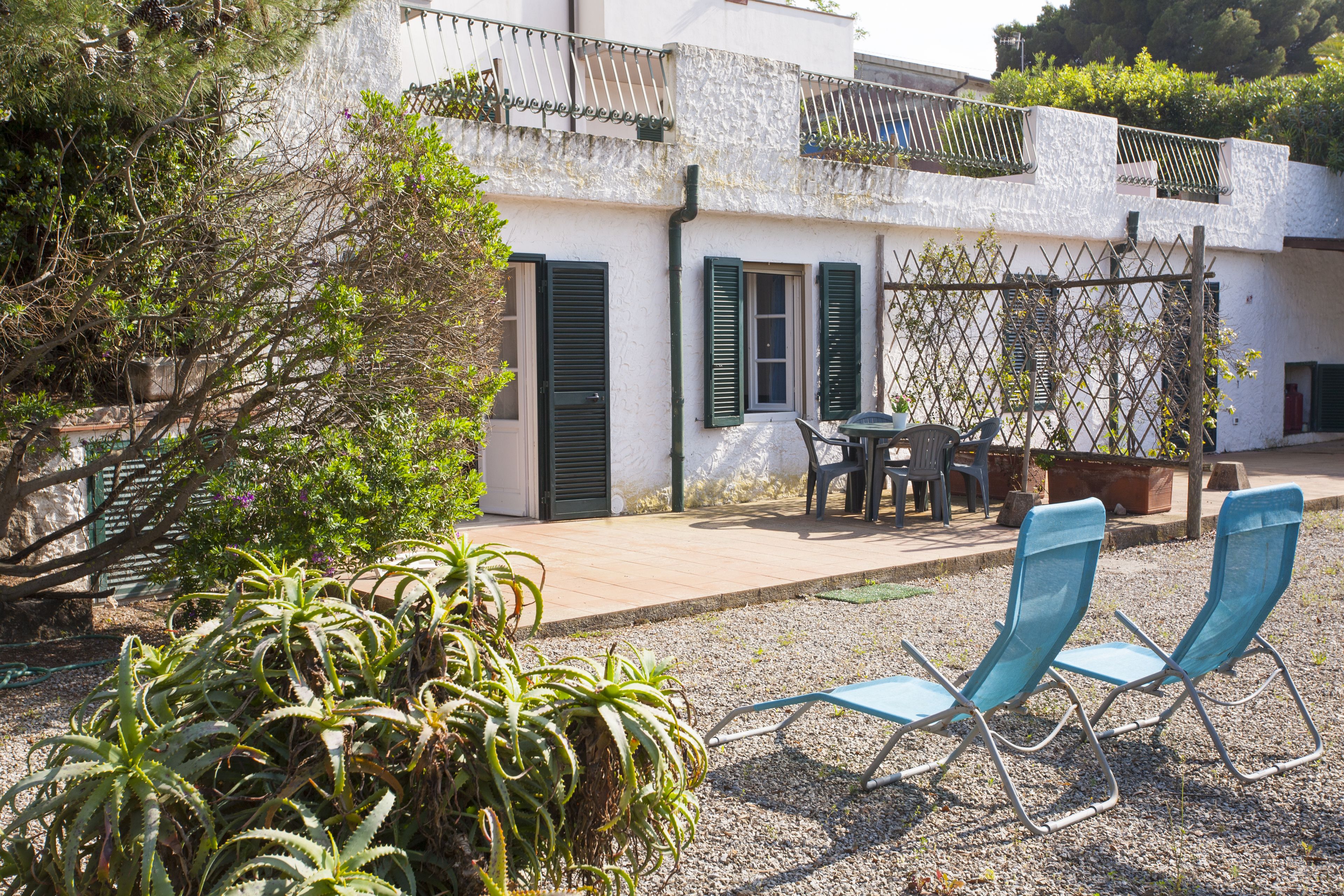Un patio con dos sillas azules, una mesa y un pequeño jardín con plantas.