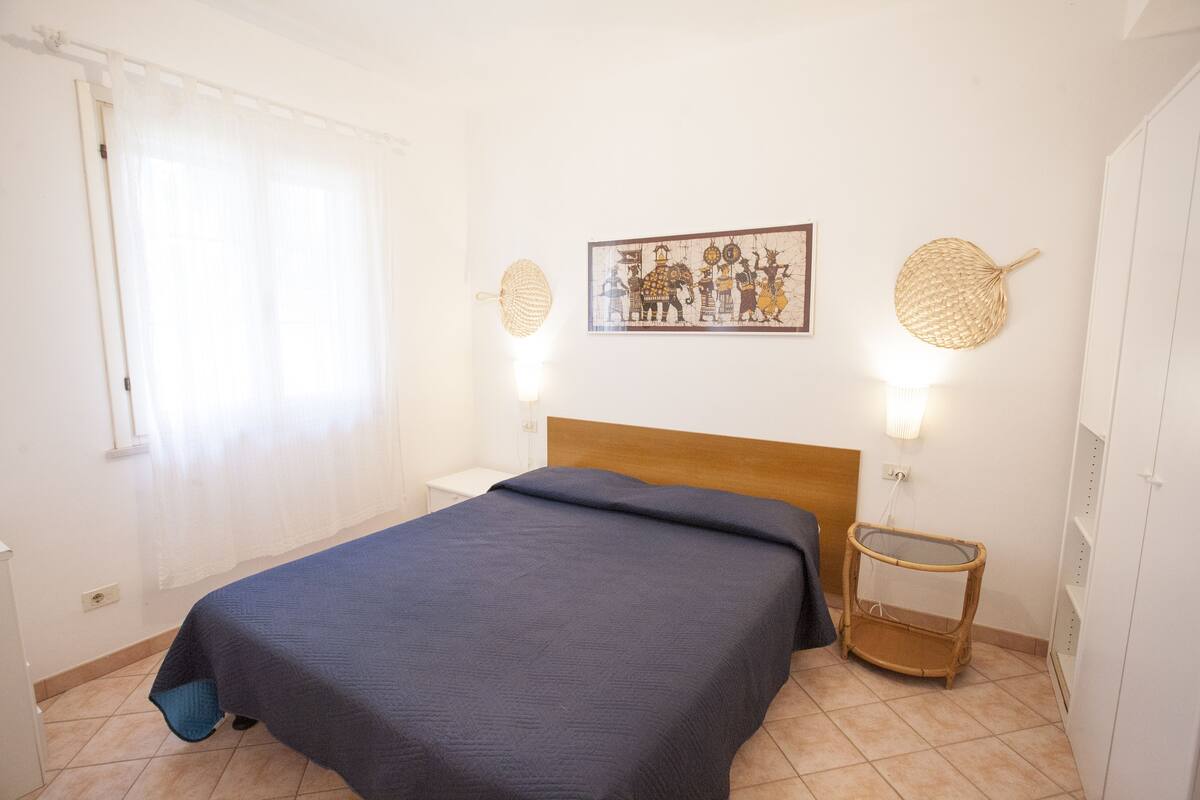 A bedroom with a bed, a nightstand, a wall-mounted lamp, and a woven basket.