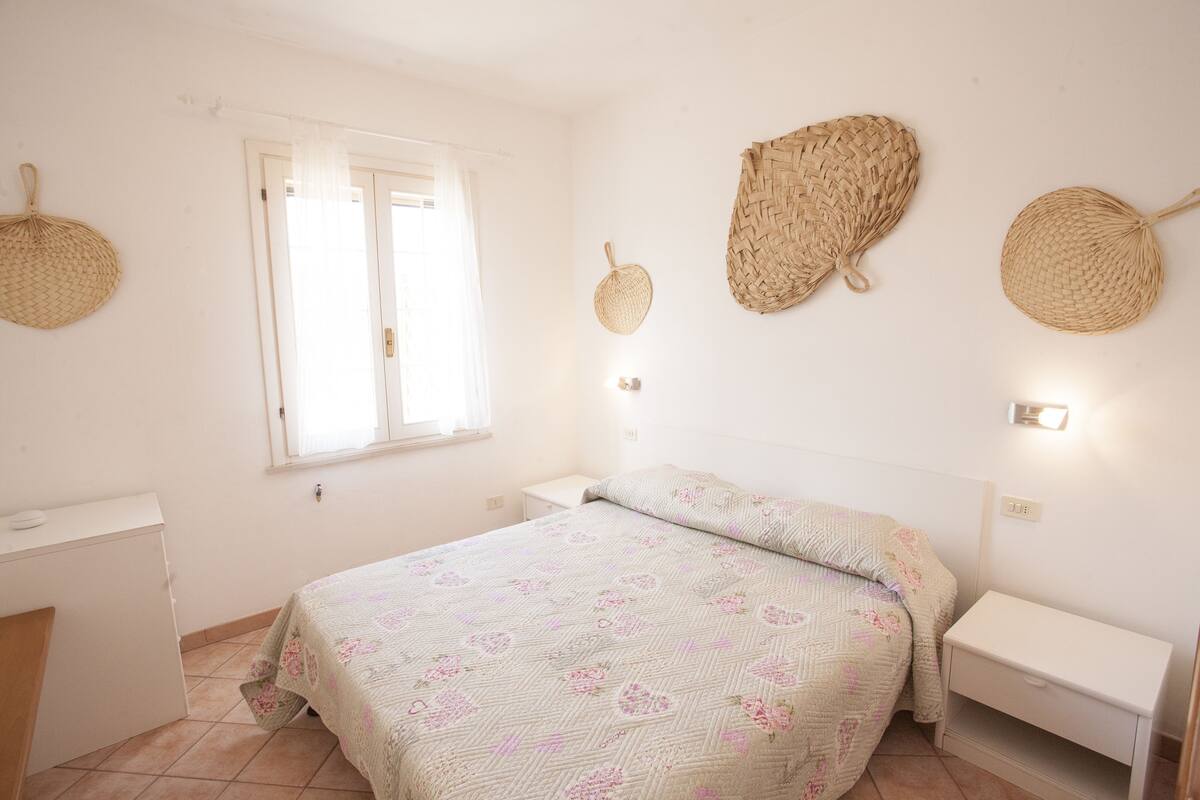 A bedroom with a bed, a desk, and a window.