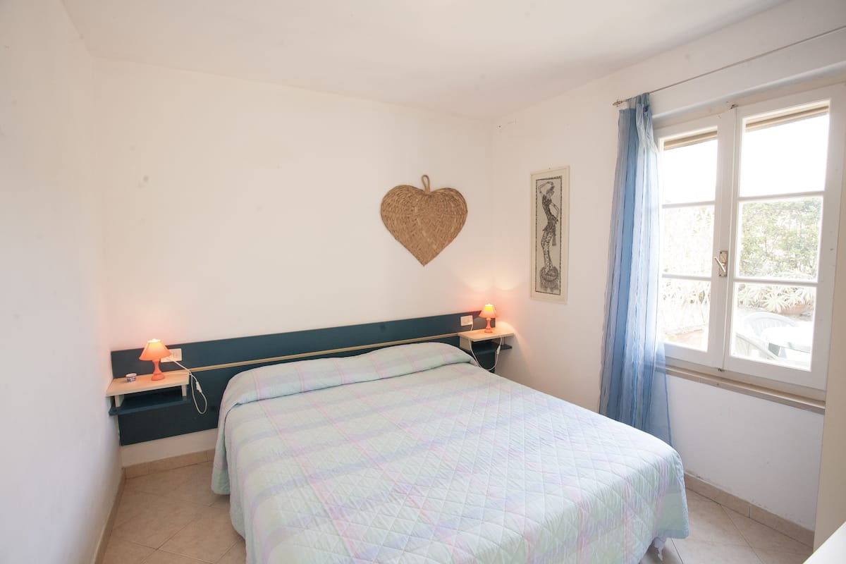A bedroom with a bed, bedside lamps, a heart-shaped wall decoration, and a window with curtains.