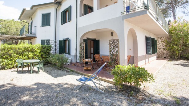 A two-story building with a balcony, outdoor seating, and a gravel driveway. - Appartamenti Arco Bianco (Capoliveri)