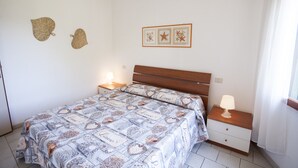A bedroom with a bed, bedside tables, a nightstand, a lamp, and wall decorations. - Appartamenti Arco Bianco (Capoliveri)