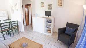 A room with a dining table, chairs, a television, and a wicker chair. - Appartamenti Arco Bianco (Capoliveri)