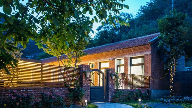 A brick house with a wooden fence, a gated entrance, and a pathway leading to the house. - Snail Home Inn (Huairou)