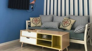 A room with a blue wall, a striped curtain, a sofa with striped cushions, a wooden coffee table, and a mounted TV. - Snail Home Inn (Huairou)