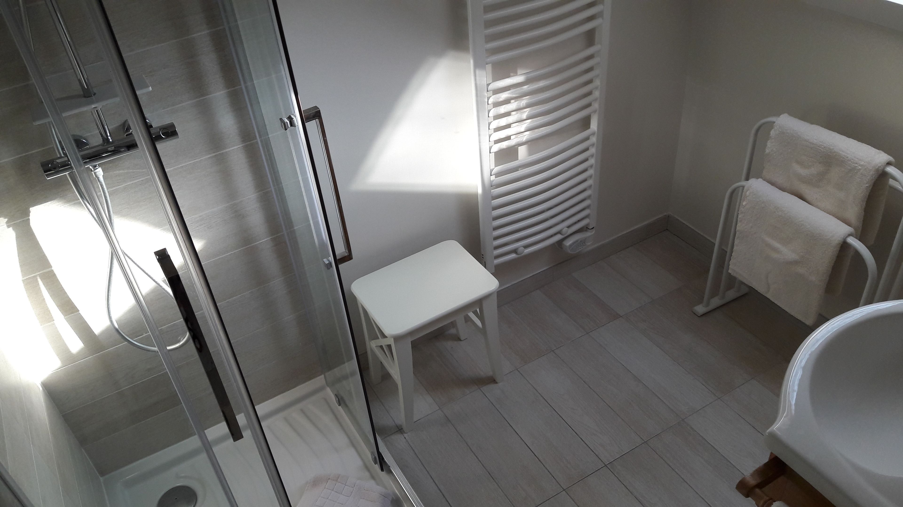 Uma casa de banho moderna com cabine de duche em vidro, um banco branco, radiador e lavatório branco.