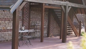 A covered outdoor seating area with a brick wall, wooden beams, and a staircase. - Le Clos des Pensées (Saint-Sauveur-d'Emalleville)