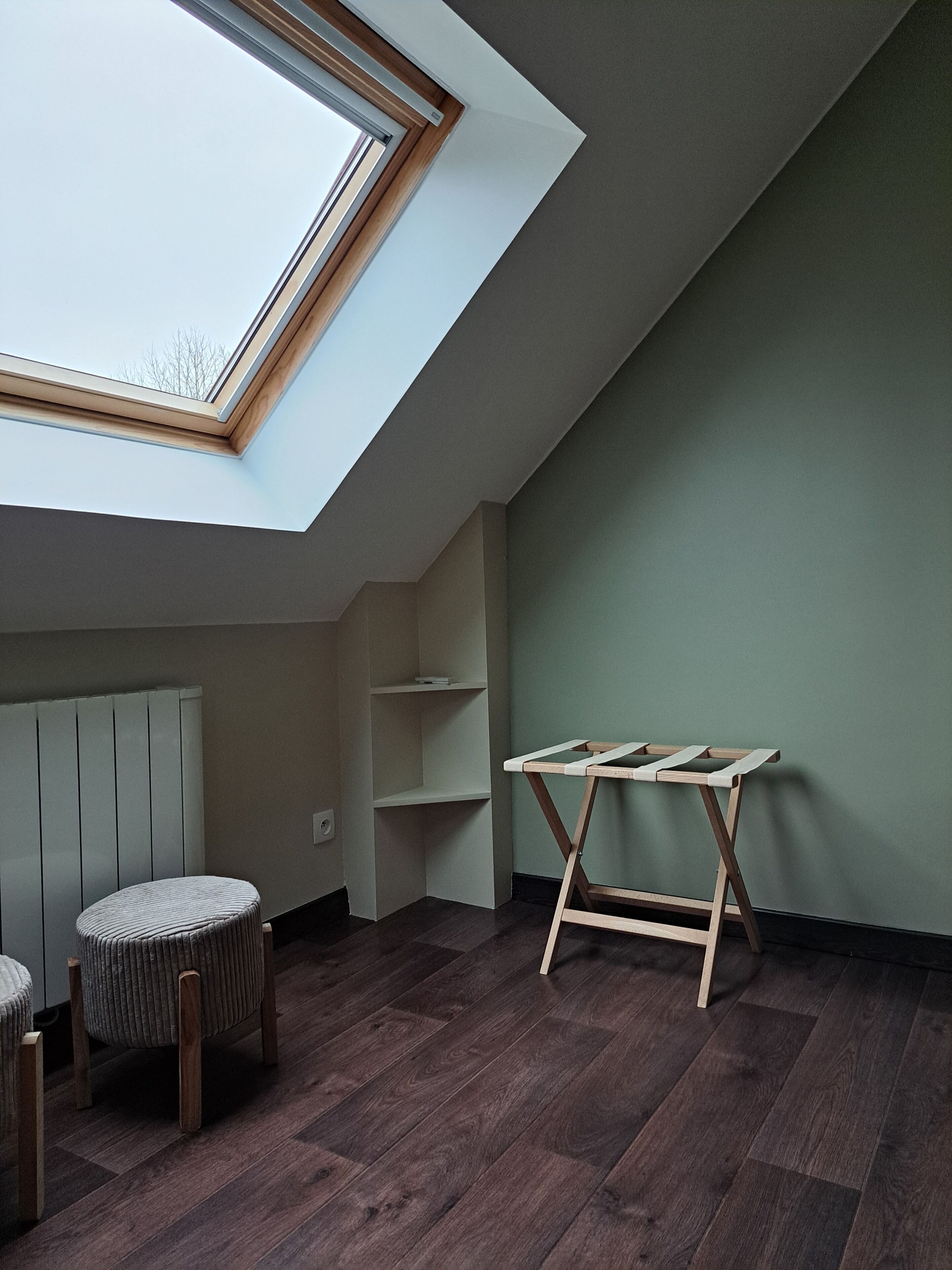 A room with a sloped ceiling, a skylight, a wooden table, a chair, and built-in shelving.