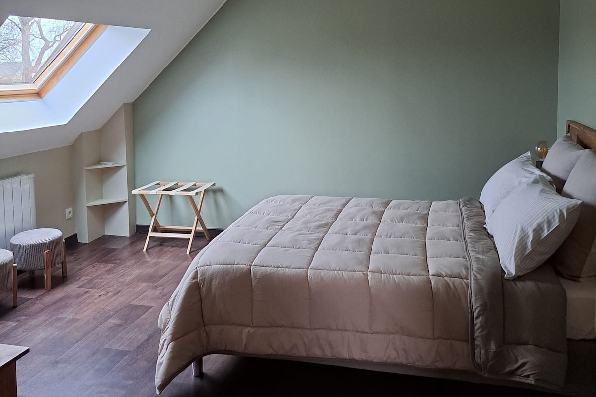 Ein Schlafzimmer mit schrägem Dach, einem Oberlicht, einem Bett mit Kissen, einem Nachttisch und einer Pendelleuchte.