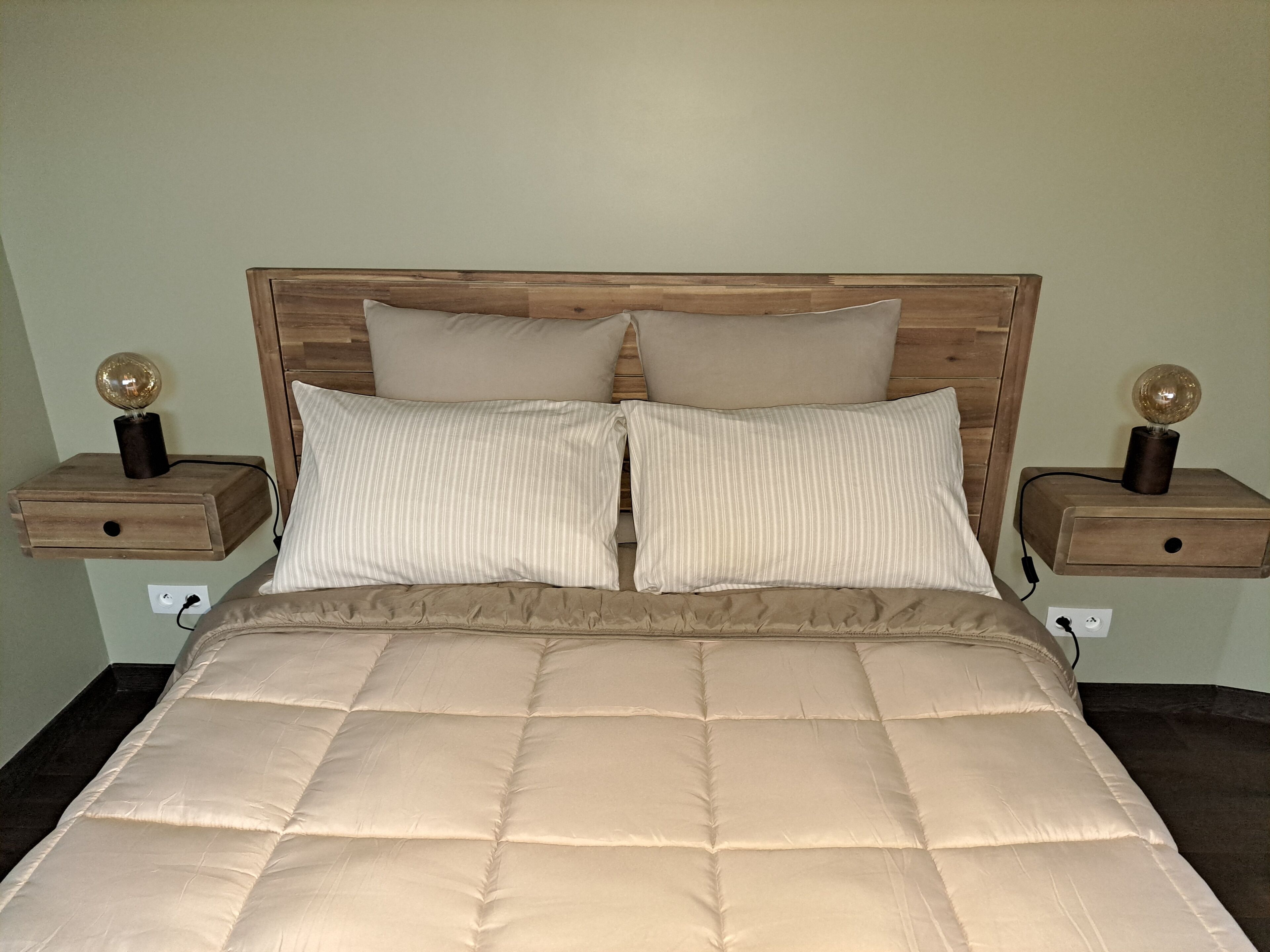 A bed with a wooden headboard, two bedside tables with lamps, and a beige quilted bedspread.