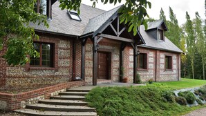 A brick house with a stone foundation, a wooden porch, and a gravel driveway. - Le Clos des Pensées (Saint-Sauveur-d'Emalleville)