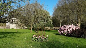 A well-maintained garden with a variety of flowering plants, a stone wall, and a building in the background. - Le Clos des Pensées (Saint-Sauveur-d'Emalleville)