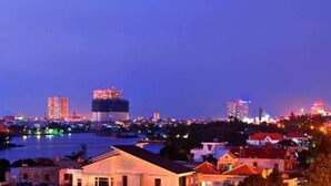 Un paisaje urbano al anochecer con edificios iluminados y un río en primer plano.