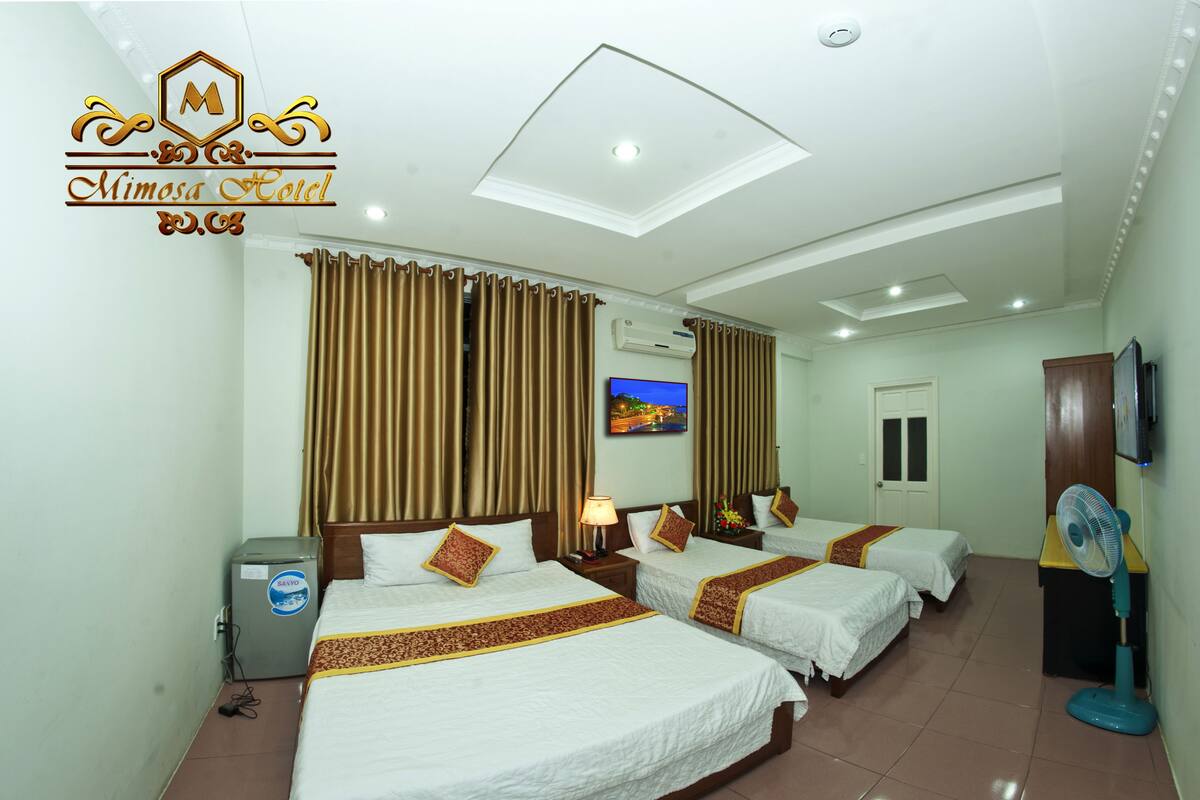 A hotel room with three beds, a ceiling fan, a TV, and a minibar.