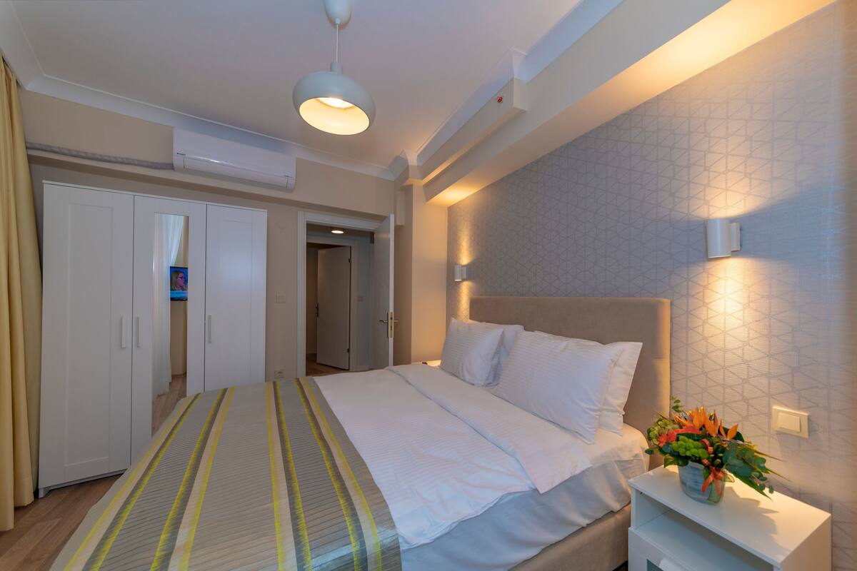 Une chambre à coucher bien rangée, avec un lit, une table de chevet et un luminaire fixé au mur.
