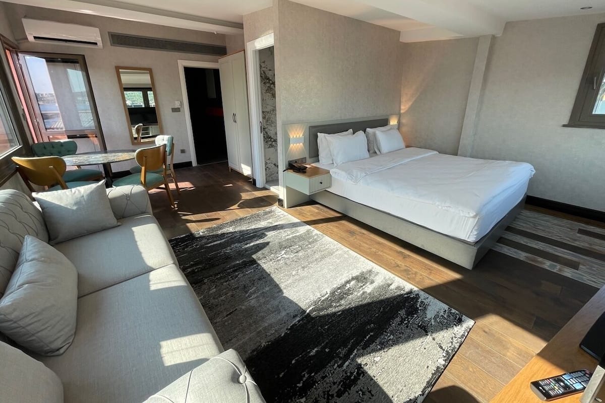 Une chambre d’hôtel moderne dotée d’un grand lit, d’un canapé, d’une table à manger avec des chaises et offrant une vue sur l’extérieur.