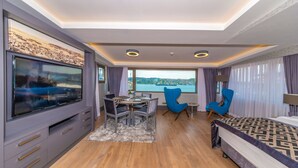 Una camera d'albergo moderna con una grande TV, un'area pranzo, un letto e vista mare.