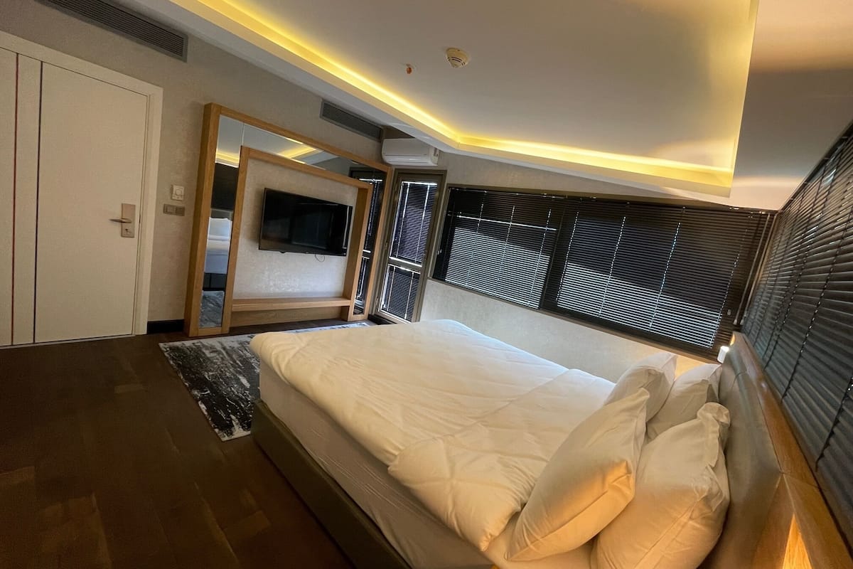 Une chambre d’hôtel moderne dotée d’un grand lit, d’un téléviseur à écran plat fixé au mur et d’une fenêtre avec des stores.
