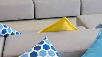 A living room with a grey sofa, blue and yellow patterned cushions, and a flat-screen TV mounted on the wall.