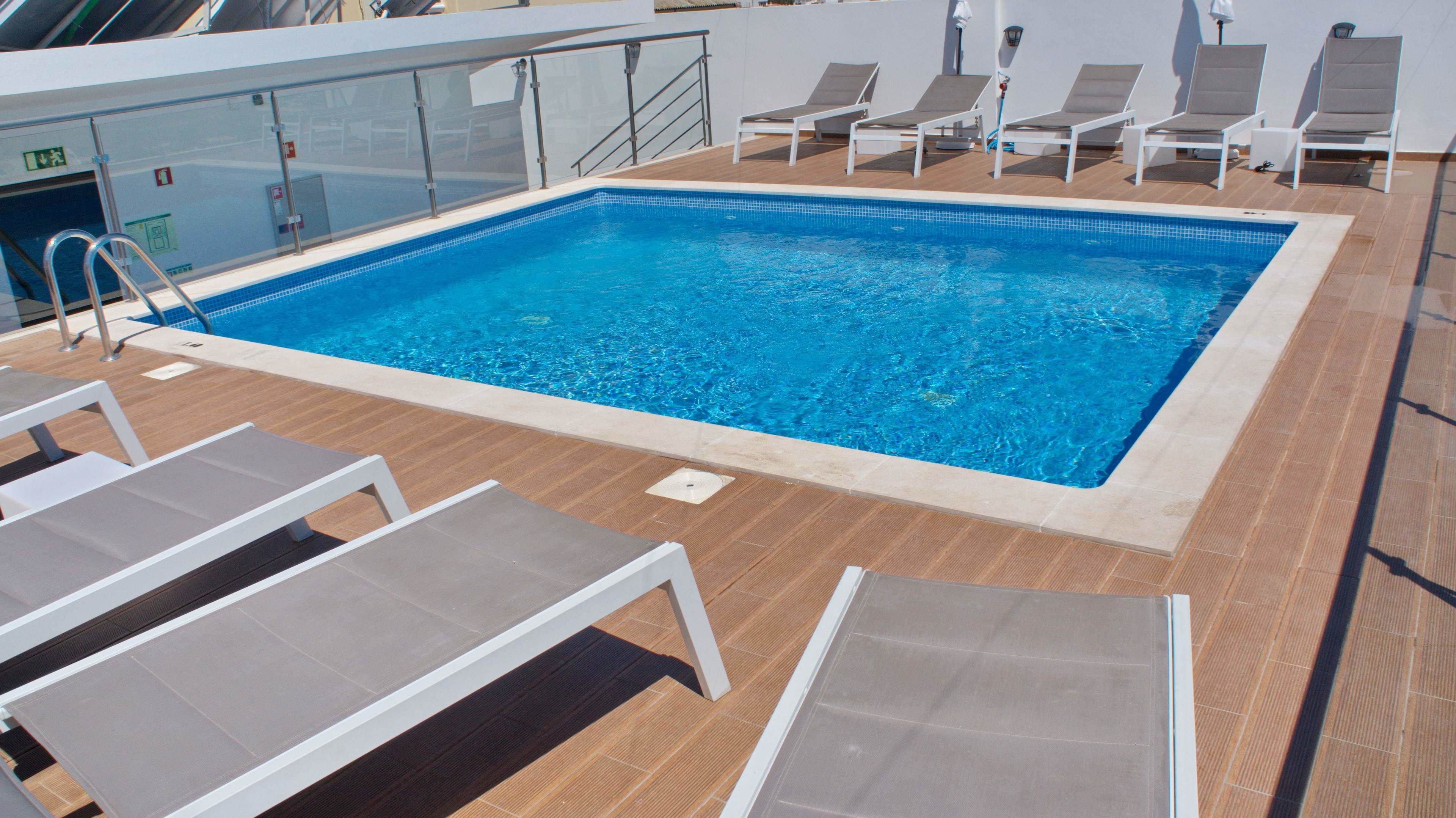 Une piscine avec des chaises longues et un poste de surveillance pour le sauveteur, le tout installé sur une terrasse.