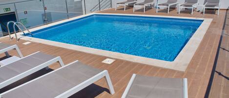 A swimming pool with sun loungers and a lifeguard stand on a deck.