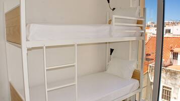 A bunk bed with white bedding and a view of the cityscape through a window.