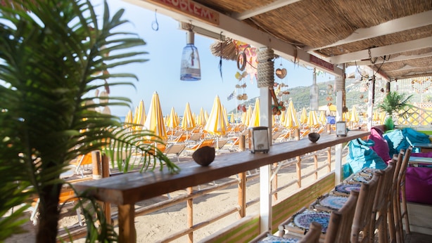 A beachside restaurant with wooden tables and chairs, umbrellas, and a view of the beach. - Residence La Palma (Andora)