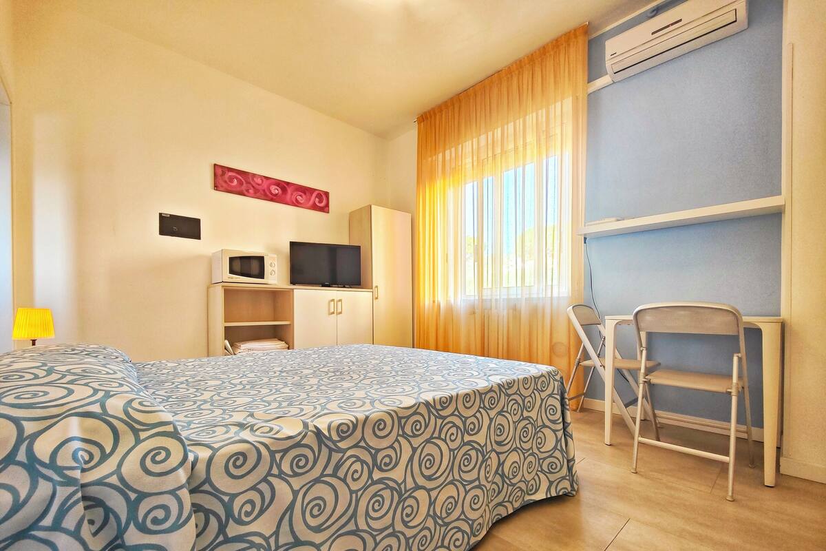 Ein Hotelzimmer mit Bett, Schreibtisch mit Stuhl, Fernseher und Klimaanlage.