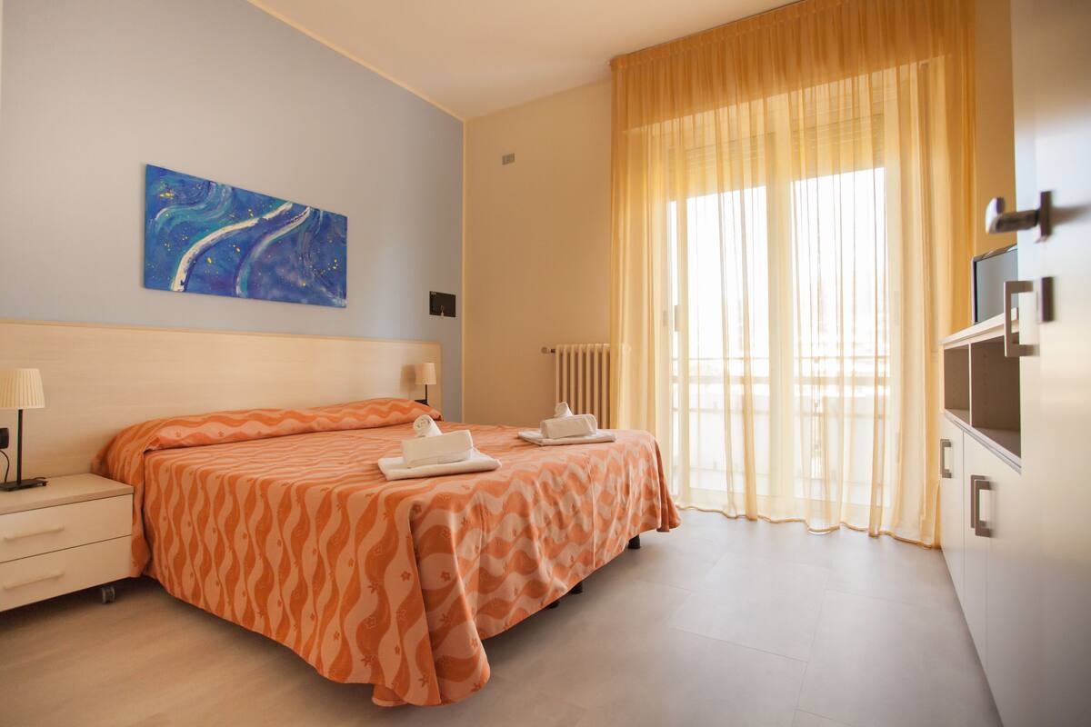 Ein Hotelzimmer mit einem Bett, einem Nachttisch, einer Lampe, einem Bild an der Wand, einem Heizkörper und einem Fernseher.