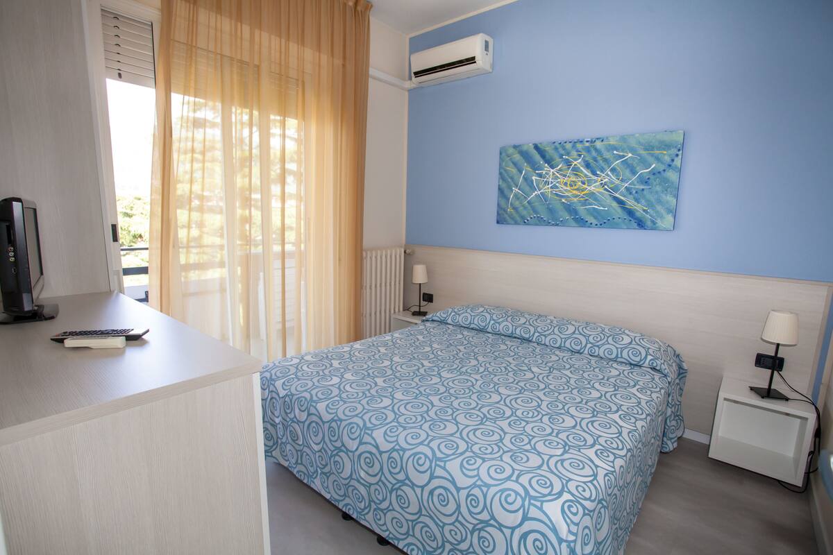 Ein Schlafzimmer mit Bett, Schreibtisch, Stuhl, Nachttisch und einer Wand-Klimaanlage.