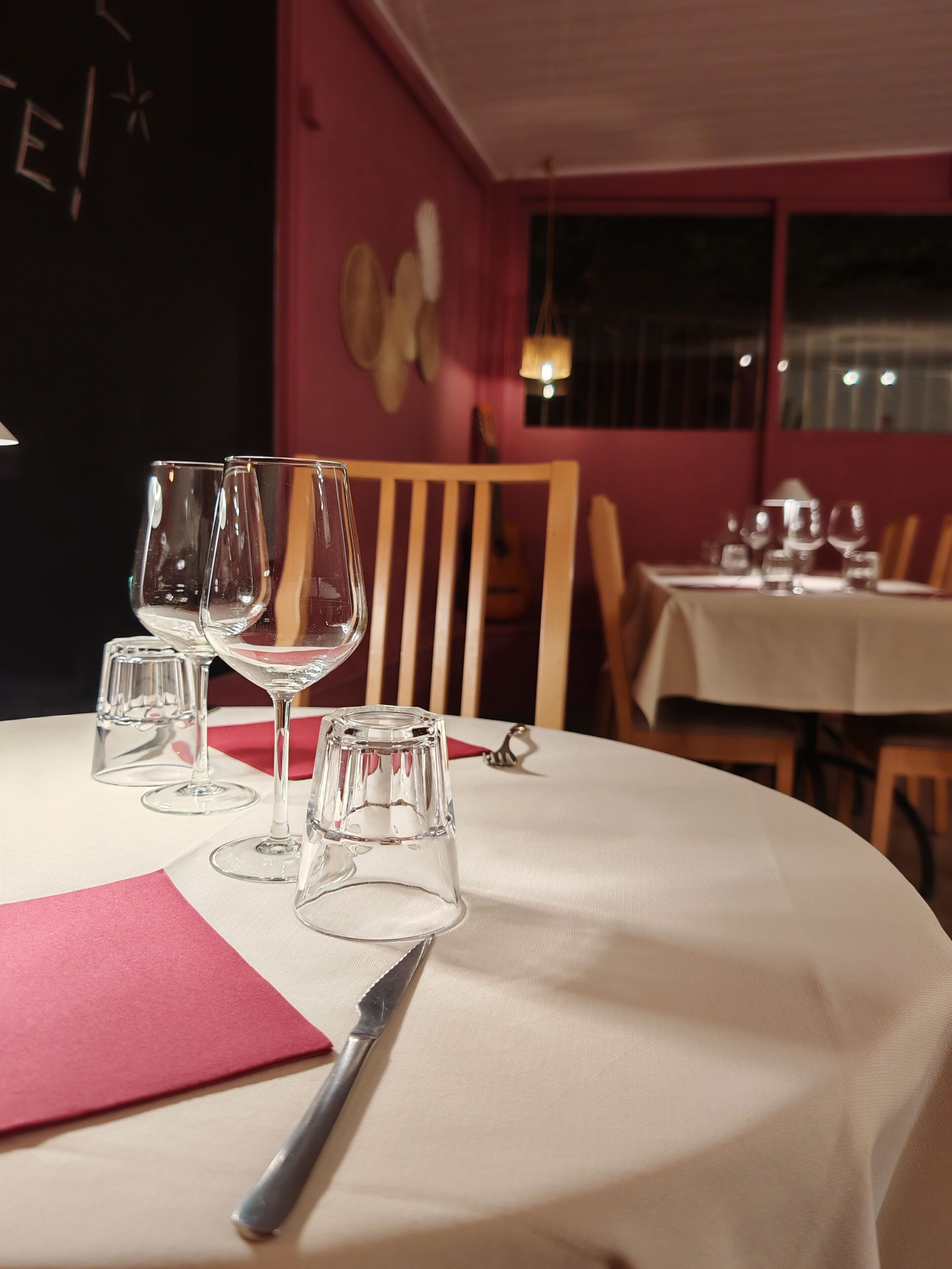 A dining table with wine glasses and a knife, a red napkin, and a wooden chair.