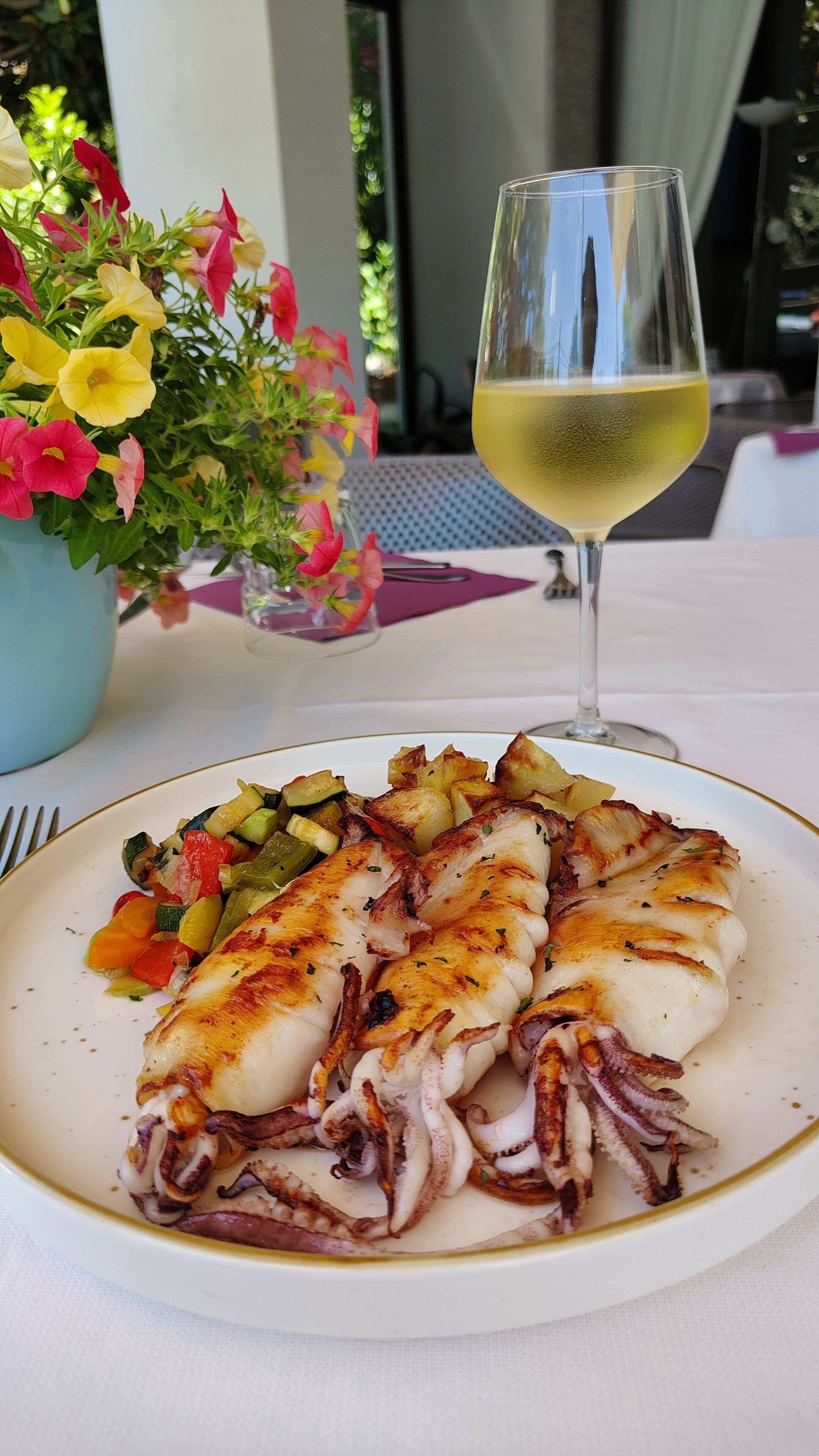A plate of grilled octopus with vegetables and a glass of white wine on a table.