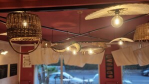 A restaurant with tables set for dining, hanging wicker lamps, and a view of parked cars outside. - Residence La Palma (Andora)
