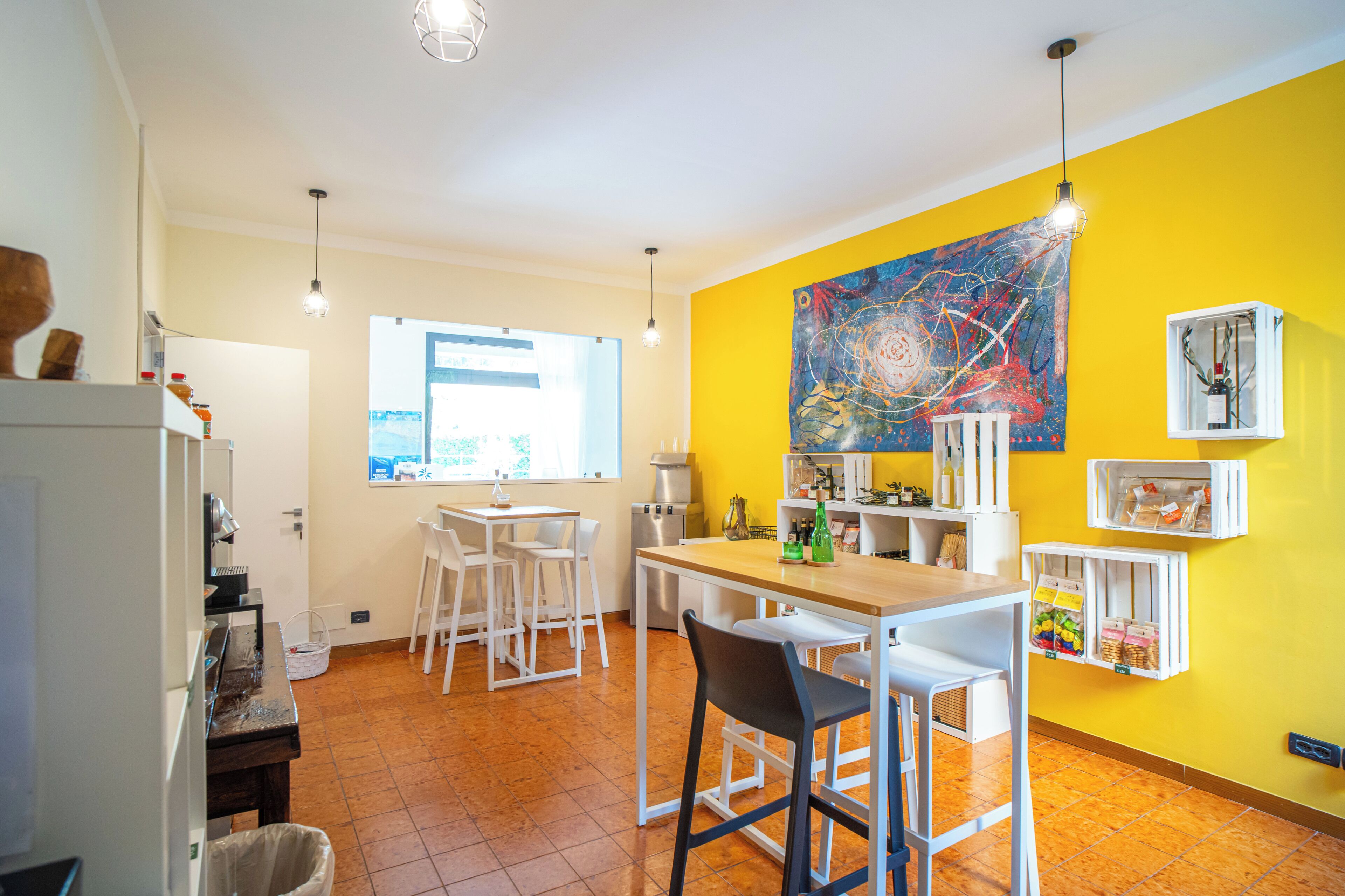 A bright kitchen with white furniture, a large window, and a yellow wall.