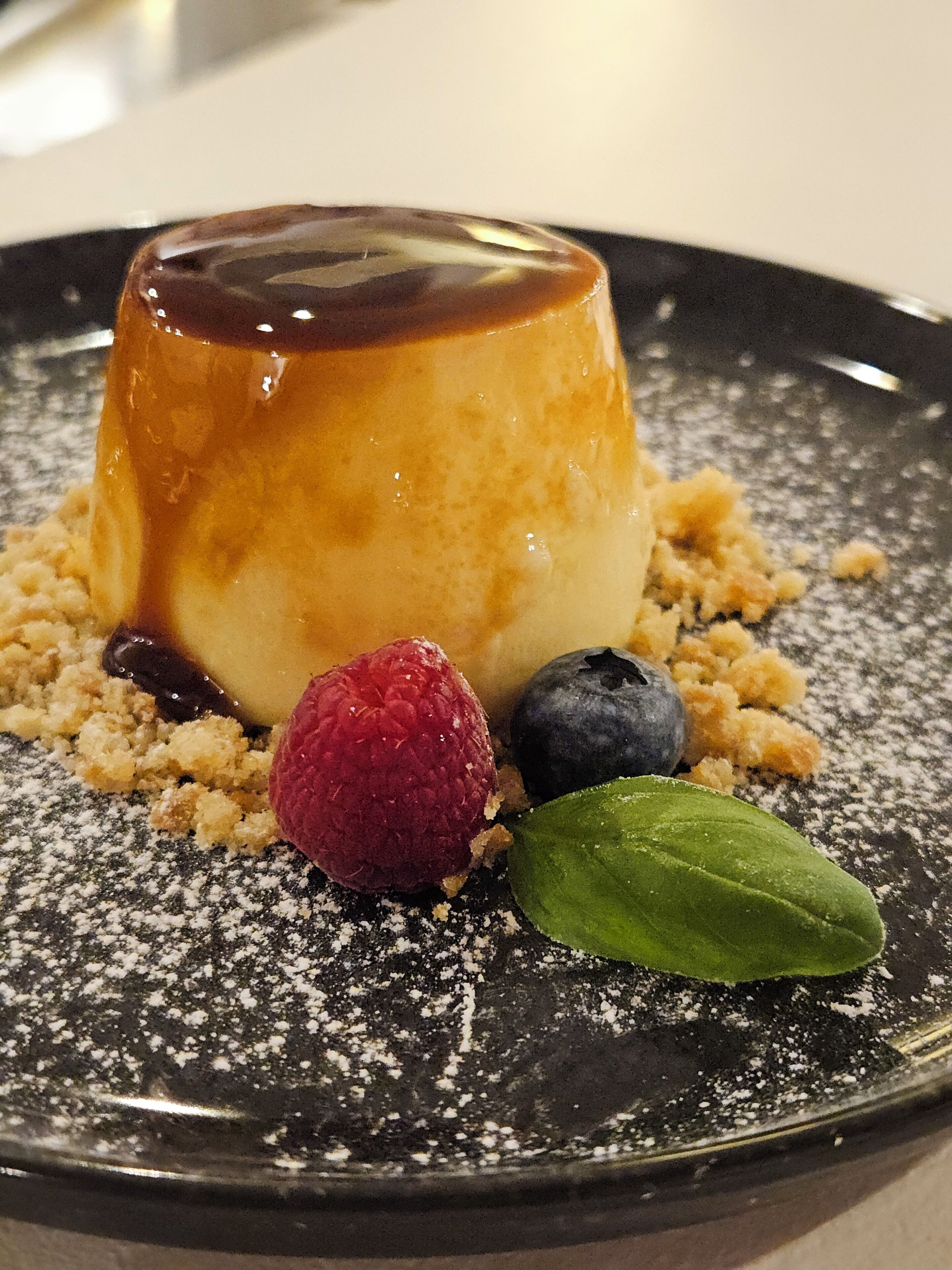 A dessert with a caramelized top, accompanied by berries and a leaf on a plate.
