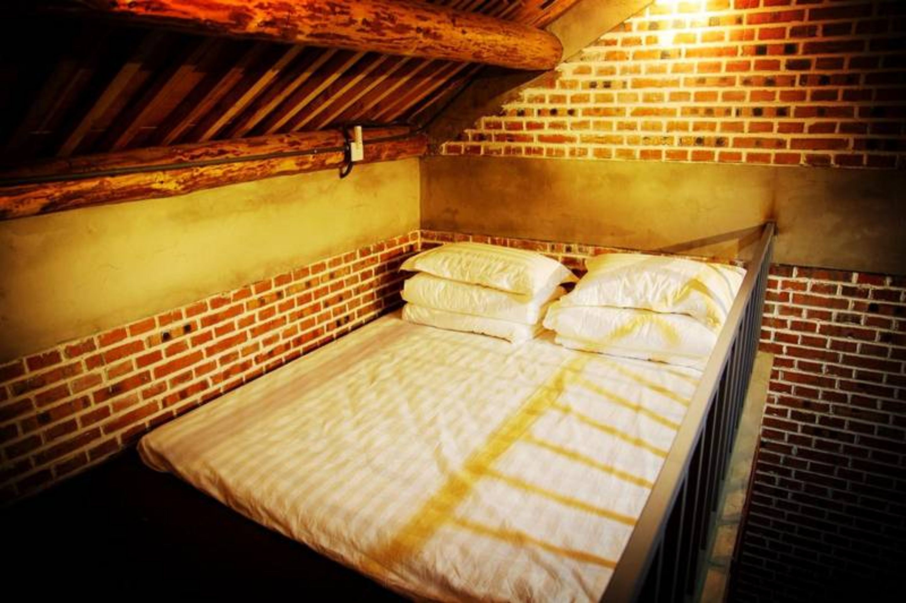 A single bed in a room with exposed brick walls and wooden beams.