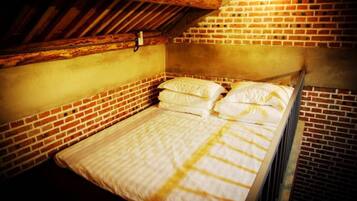 A single bed in a room with exposed brick walls and wooden beams.