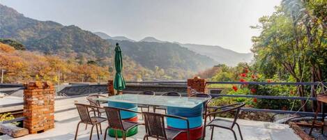 Una terraza con mesa y sillas de vidrio, rodeada por un muro de ladrillo y vistas a montañas.