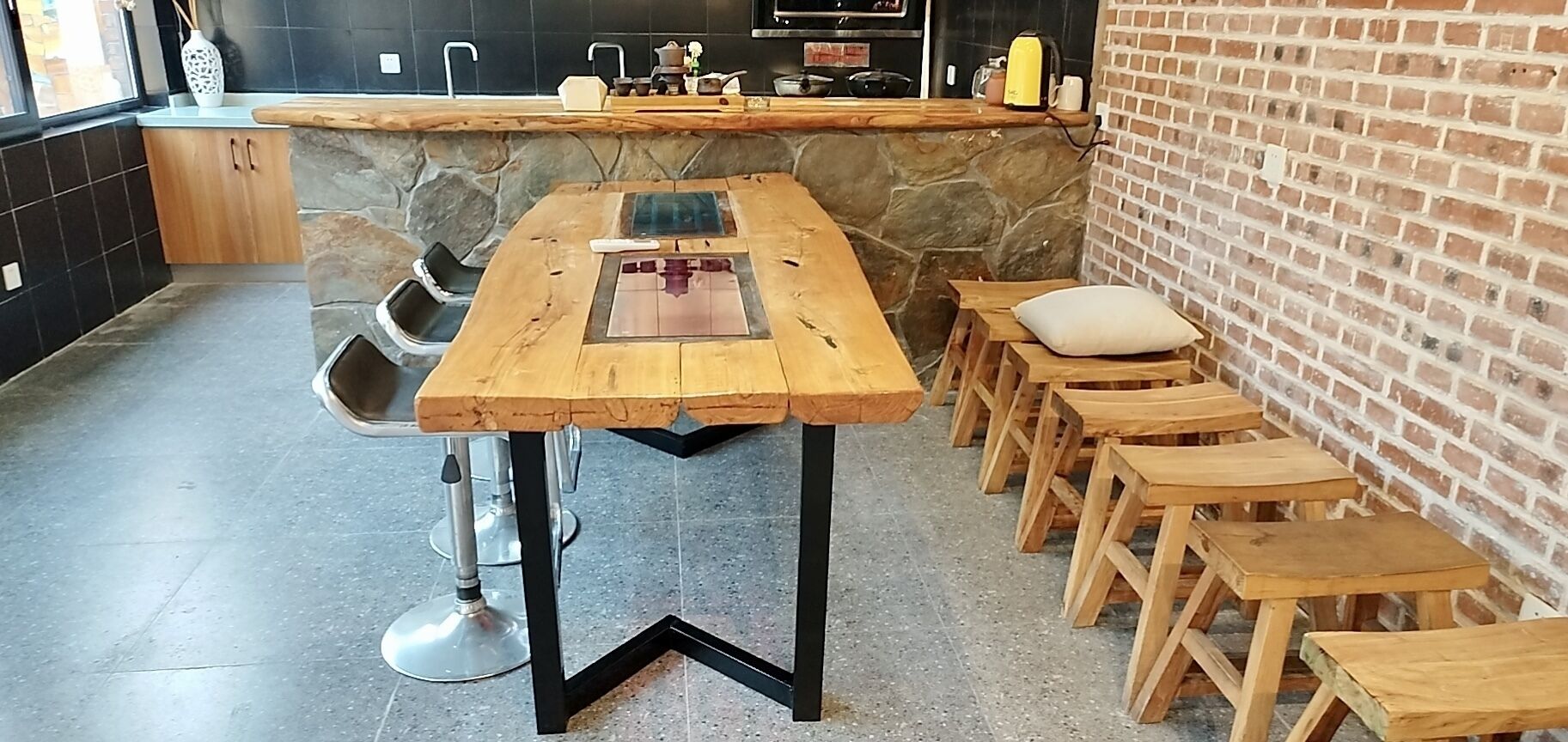 A kitchen with a long wooden table, black metal legs, and a brick wall.