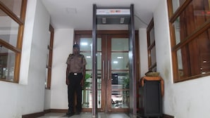 A security guard standing in front of a glass door with a digital clock above it.